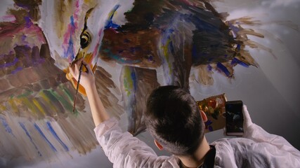 Artist designer draws an eagle on wall. Craftsman decorator paints picture with acrylic oil color...