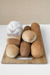 A lot of different bread lies on a wooden board on a light background, vertical photo, there is a place for text, minimalism