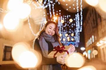 With gift box. Cute and happy asian young woman outdoors in the city celebrates New year