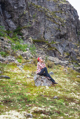 Naklejka na ściany i meble Happy traveler trekking woman sitting on the stone in the tundra