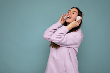 Pretty positive smiling young brunette woman wearing light purple hoodie isolated over blue...