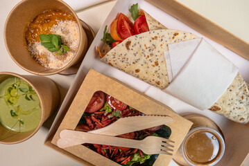 Chicken tortilla with tomato, carrot and beet salad, pumpkin soup and mango and pineapple dessert packed in degradable packaging for delivery