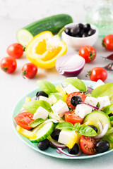 Fresh homemade greek salad with basil leaves on a plate and ingredients for cooking on the table. Domestic life. Vertical view. Close-up