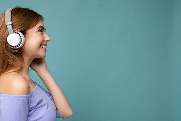 Side-profile portrait photo of beautiful positive smiling young blonde woman wearing blue crop top...