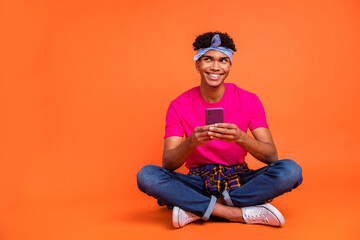 Full length body size photo of curious dreamy hipster reading news with mobile phone isolated vivid orange color background copyspace