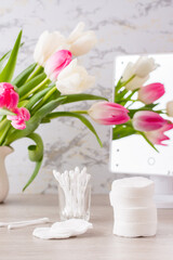 Personal hygiene, cleanliness and skin care. Cotton pads and swabs  on a table in front of a mirror and a bouquet of tulips. Vertical view