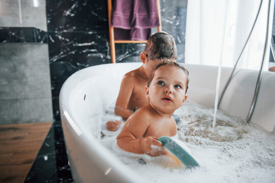 Two Kids Having Fun And Washing Themselves In The Bath At Home. Helping Each Other