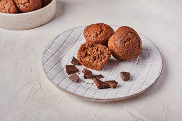 Homemade chocolate cupcakes and pieces of chocolate in textured plate on wooden light background, top view, copy space