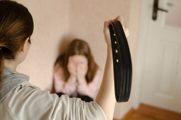 Domestic violence against children. Mom with a belt stands in front of the child. Daughter crying in the corner