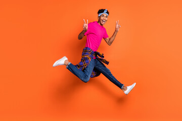 Fototapeta na wymiar Full size photo of young handsome funky positive afro man jumping showing v-sign isolated on orange color background