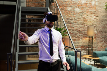 A man office manager in formal clothing wearing virtual reality vr glasses swiping scrolling online images in modern office. Augmented reality concept. People and technology.
