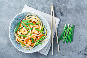 Udon noodles and wok with shrimps, peppers and onions in a plate on a napkin and chopsticks on the table. Chinese food. Top view