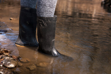 A farmer's dirty rubber boots are walking along a rainy road. The farmer girl crosses the river. 
