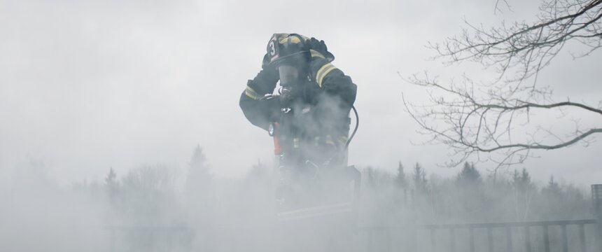 Silhouette of American female firefighter in traditional helmet and full gear standing in the smoke. Shot with 2x anamorphic lens