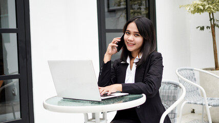 Asian young business woman working on computer and talking on smartphone in office
