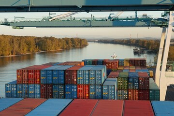 Columbia river surrounded by trees and bushes with container terminal with gantry cranes ready for...
