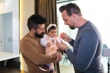 gay couple feeding their young daughter in the kitchen while the little girl watches the food attentively