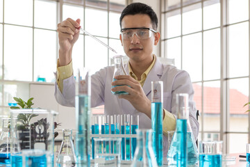 Young and good looking researcher wearing safety protective eyesglassed working in laboratory with blue liquid in test tube