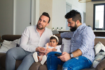 Obraz premium gay couple and their daughter sitting on the sofa watching television. The girl watches the cartoons attentively.
