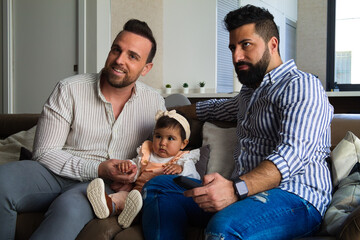 gay couple and their daughter sitting on the sofa watching television. The girl watches the cartoons attentively.