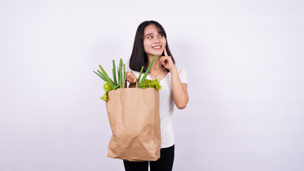 Fototapeta na wymiar Asian woman thinking with paper bag of fresh vegetables with isolated white background