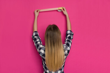 Young Woman Is Holding Painter's Tape On Pink Wall. Rear View.