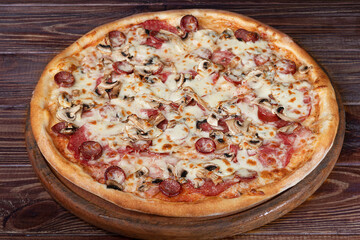 Pizza with bacon cheese and herbs on a wooden plate with cheese and cherry tomatoes. On a wooden background.