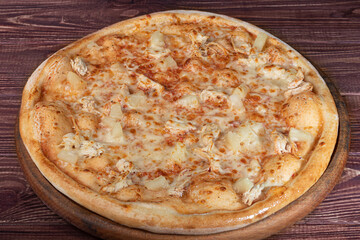 Pizza with bacon cheese and herbs on a wooden plate with cheese and cherry tomatoes. On a wooden background.