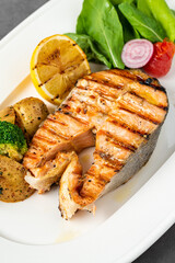 plate of grilled salmon steak with vegetables on dark stone table