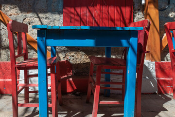 Fototapeta na wymiar Old wooden blue table and red chairs outside. Mediterranean local cafe in small town. Cozy family restaurant in Europe without client. Empty table.
