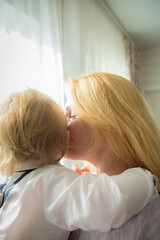 Fototapeta premium Mom hugs and kisses the baby standing by the window