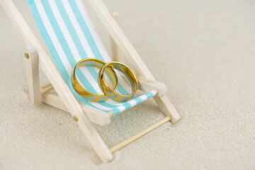 Two golden wedding rings close up on a sun lounger on sand. Wedding on the beach invitation card...