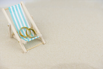 Fototapeta na wymiar Two golden wedding rings close up on a sun lounger on sand. Wedding on the beach invitation card concept.