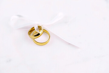 Two golden wedding rings close up with ribbon on white background. Wedding invitation card concept. 