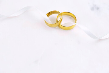 Two golden wedding rings close up with ribbon on white background. Wedding invitation card concept. 