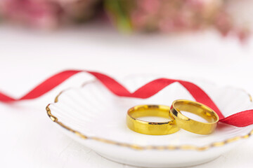 Two golden wedding rings close up with flowers on white background. Wedding invitation card concept. 