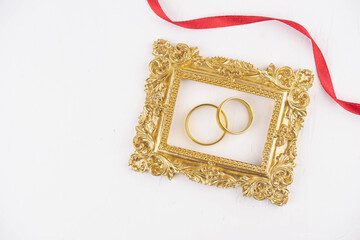 Two golden wedding rings close up with wooden picture frame on white background. Wedding invitation card concept. 