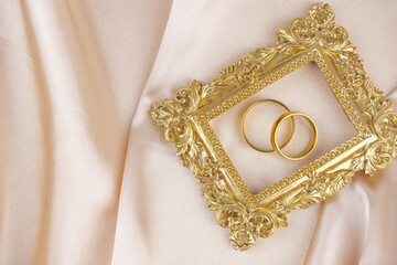 Two golden wedding rings close up with wooden picture frame on the cloth. Wedding invitation card concept. 