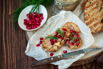 Fresh homemade chicken liver pate on bread with pomegranate seeds and dill over rustic wooden background. Soft focus