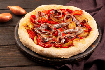 Spanish coca with onion, bell pepper and anchovy on a dark wooden background