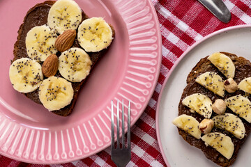 Toasted whole wheat bread with chocolate nuts paste nutella topping, banana, chia seeds, almonds and hazelnuts toast. Healthy proper nutrition for breakfast