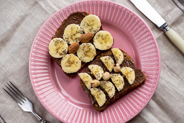 Toasted whole wheat bread with chocolate nuts paste nutella topping, banana, chia seeds, almonds and hazelnuts toast. Healthy proper nutrition for breakfast