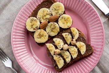 Toasted whole wheat bread with chocolate nuts paste nutella topping, banana, chia seeds, almonds and hazelnuts toast. Healthy proper nutrition for breakfast