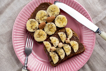 Toasted whole wheat bread with chocolate nuts paste nutella topping, banana, chia seeds, almonds and hazelnuts toast. Healthy proper nutrition for breakfast