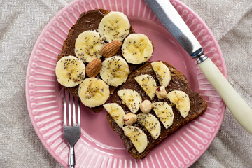 Toasted whole wheat bread with chocolate nuts paste nutella topping, banana, chia seeds, almonds and hazelnuts toast. Healthy proper nutrition for breakfast