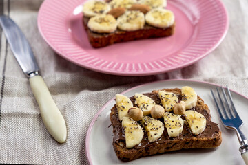 Toasted whole wheat bread with chocolate nuts paste nutella topping, banana, chia seeds, almonds and hazelnuts toast. Healthy proper nutrition for breakfast