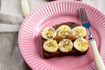 Toasted whole wheat bread with chocolate nuts paste nutella topping, banana, chia seeds, almonds and hazelnuts toast. Healthy proper nutrition for breakfast