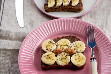 Toasted whole wheat bread with chocolate nuts paste nutella topping, banana, chia seeds, almonds and hazelnuts toast. Healthy proper nutrition for breakfast