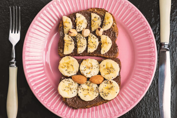 Toasted whole wheat bread with chocolate nuts paste nutella topping, banana, chia seeds, almonds and hazelnuts toast. Healthy proper nutrition for breakfast