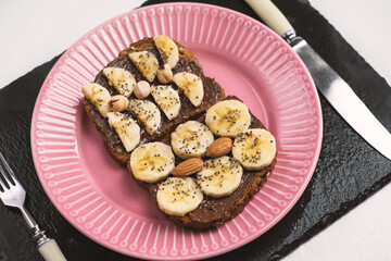 Toasted whole wheat bread with chocolate nuts paste nutella topping, banana, chia seeds, almonds and hazelnuts toast. Healthy proper nutrition for breakfast